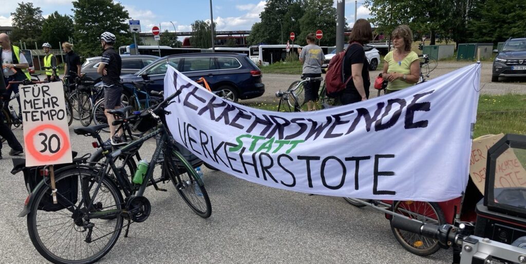 Foto der Auftaktkundgebung. Es ist ein Plakat mit der Aufschrift "Für mehr Tempo 30"und ein Banner mit der Aufschrift "Verkehrswende statt Verkehrstote" zu sehen.